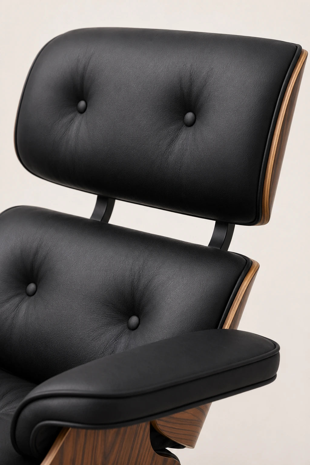Close-up of black leather button-tufted cushions, padded armrest and walnut edging on the lounge chair