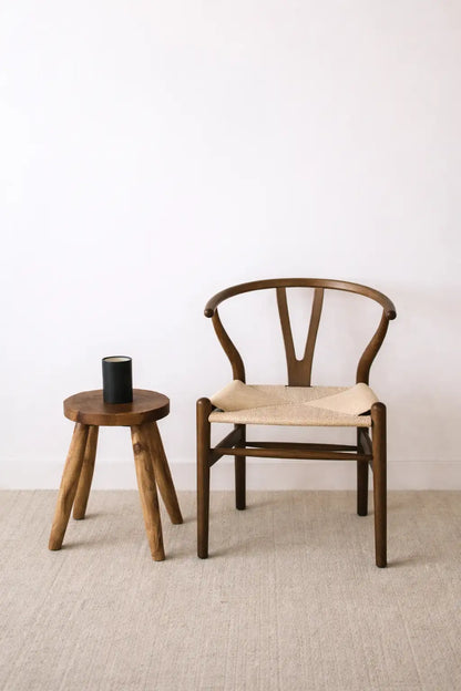 Mid-century wooden wishbone chair UK with natural rattan seat beside rustic wooden stool in minimalist Scandinavian interior.