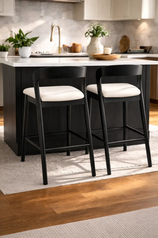 Black solid wood bar stools with cream upholstered seats positioned at a modern kitchen island in a bright contemporary interior.