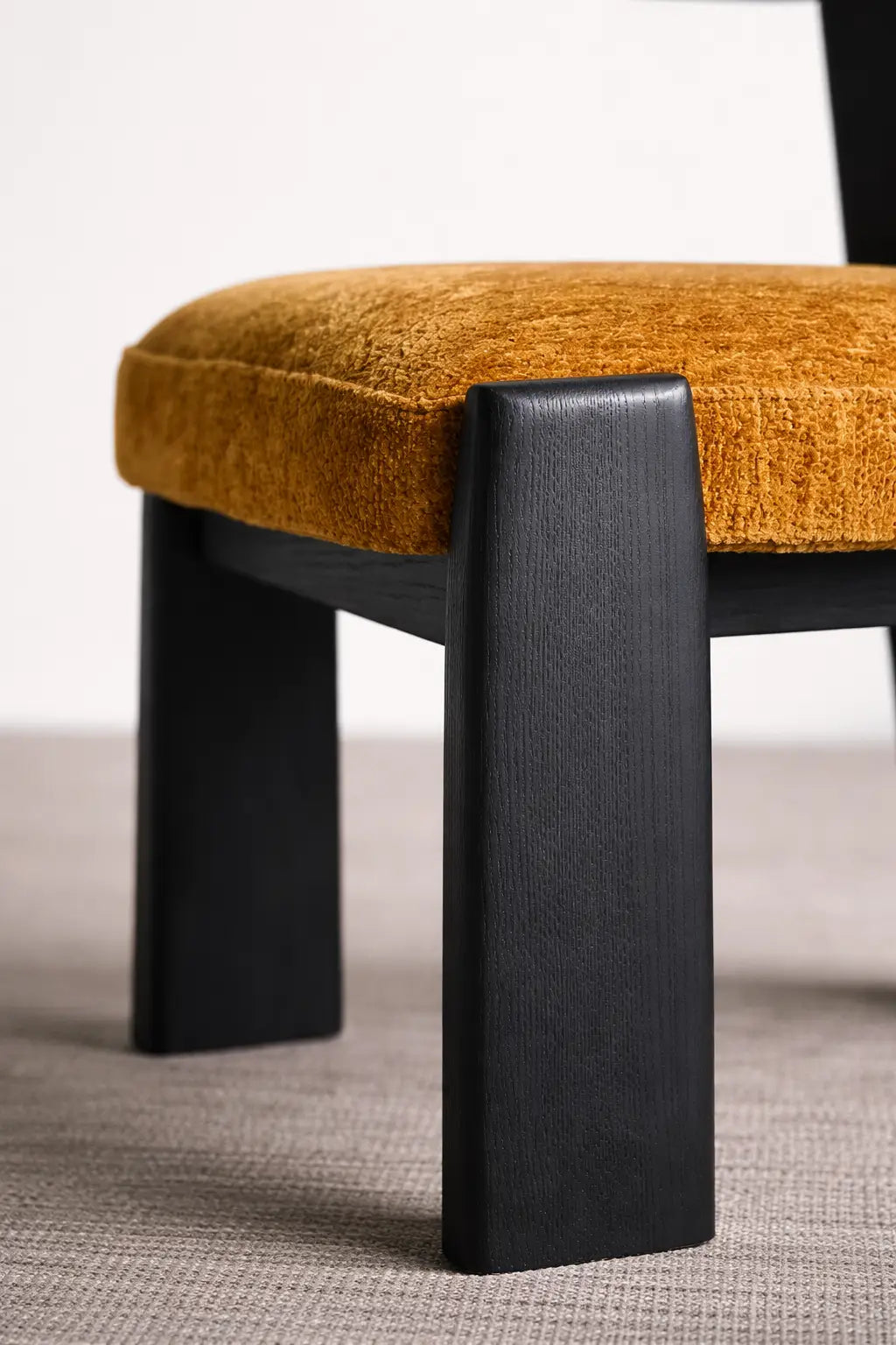 Chair with mustard yellow cushion and black legs on a neutral background
