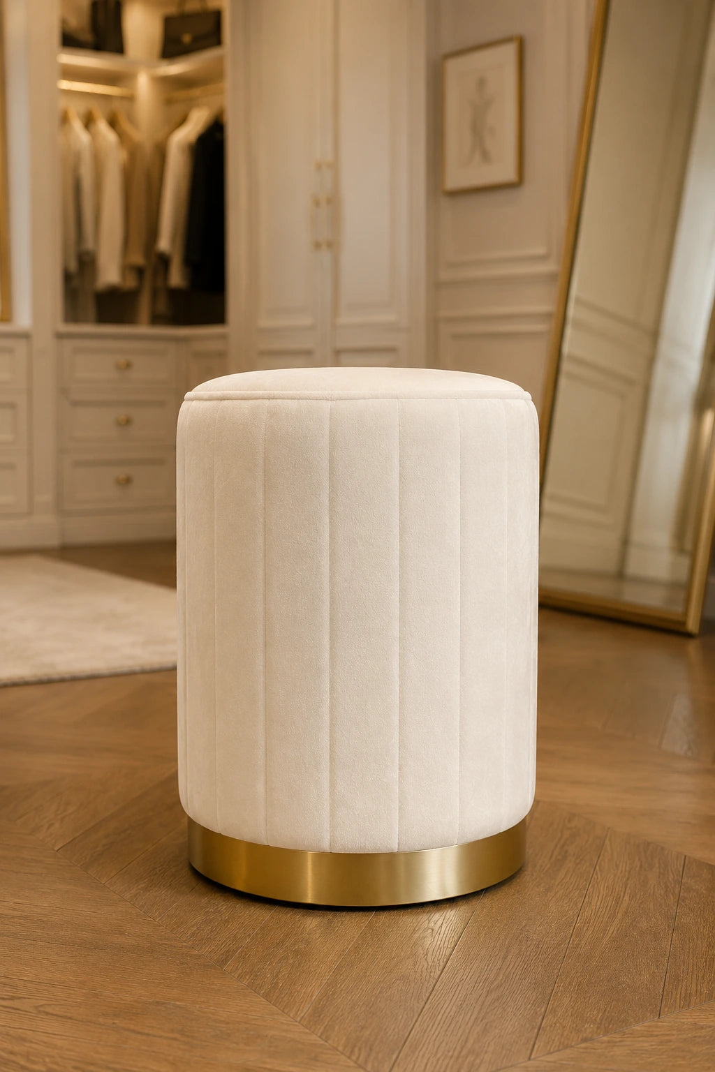 White upholstered stool with gold base on a wooden floor in a room with mirrors and cabinets.
