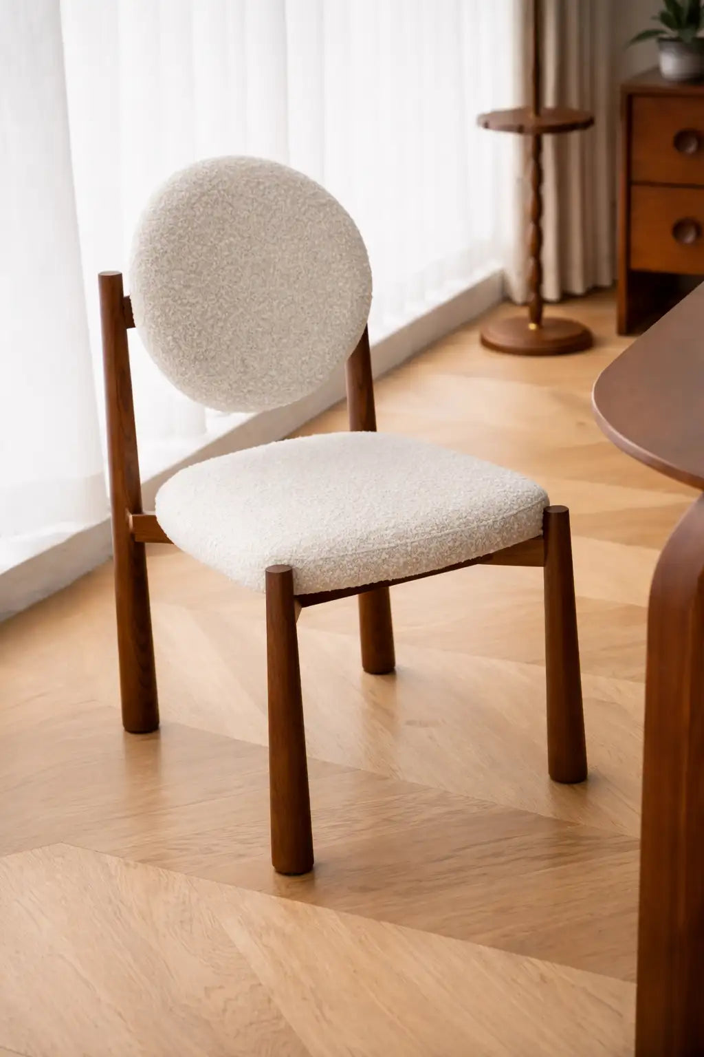 Chair with wooden frame and white cushioned seat and backrest in a room with light wood flooring and a curtain.