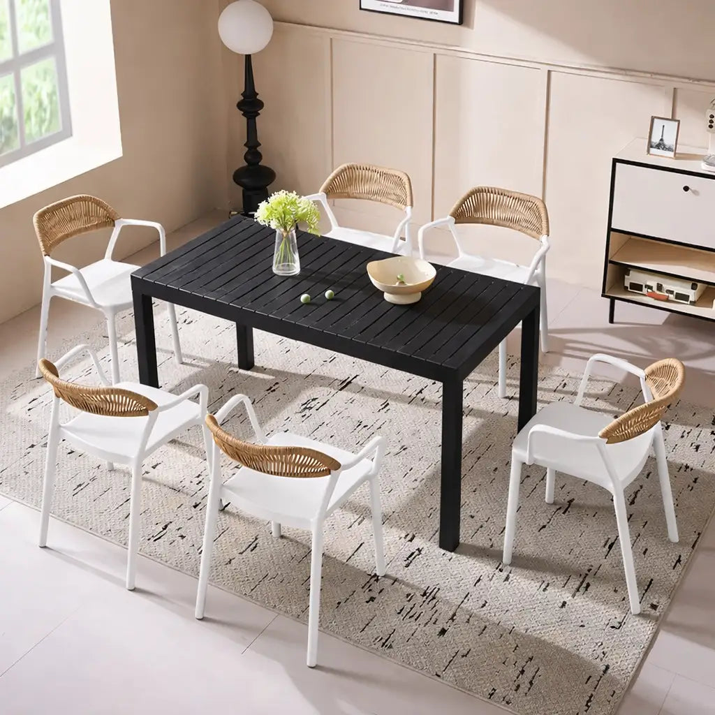 Black dining table with white chairs and wicker backrests in a modern living room.