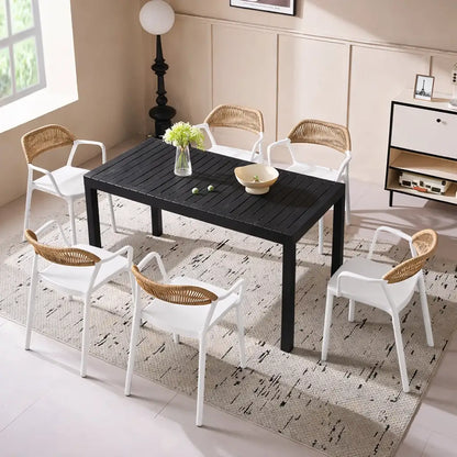 Black dining table with white chairs and wicker backrests in a modern living room.