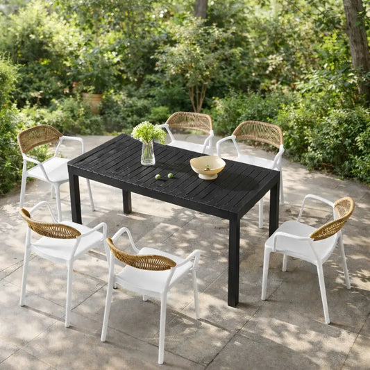 Outdoor dining set with a black table and white chairs with wicker backs on a patio.