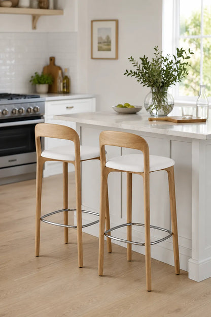Pair of oak wooden bar stools with white seats and chrome footrests beside a dark kitchen island in a modern UK home