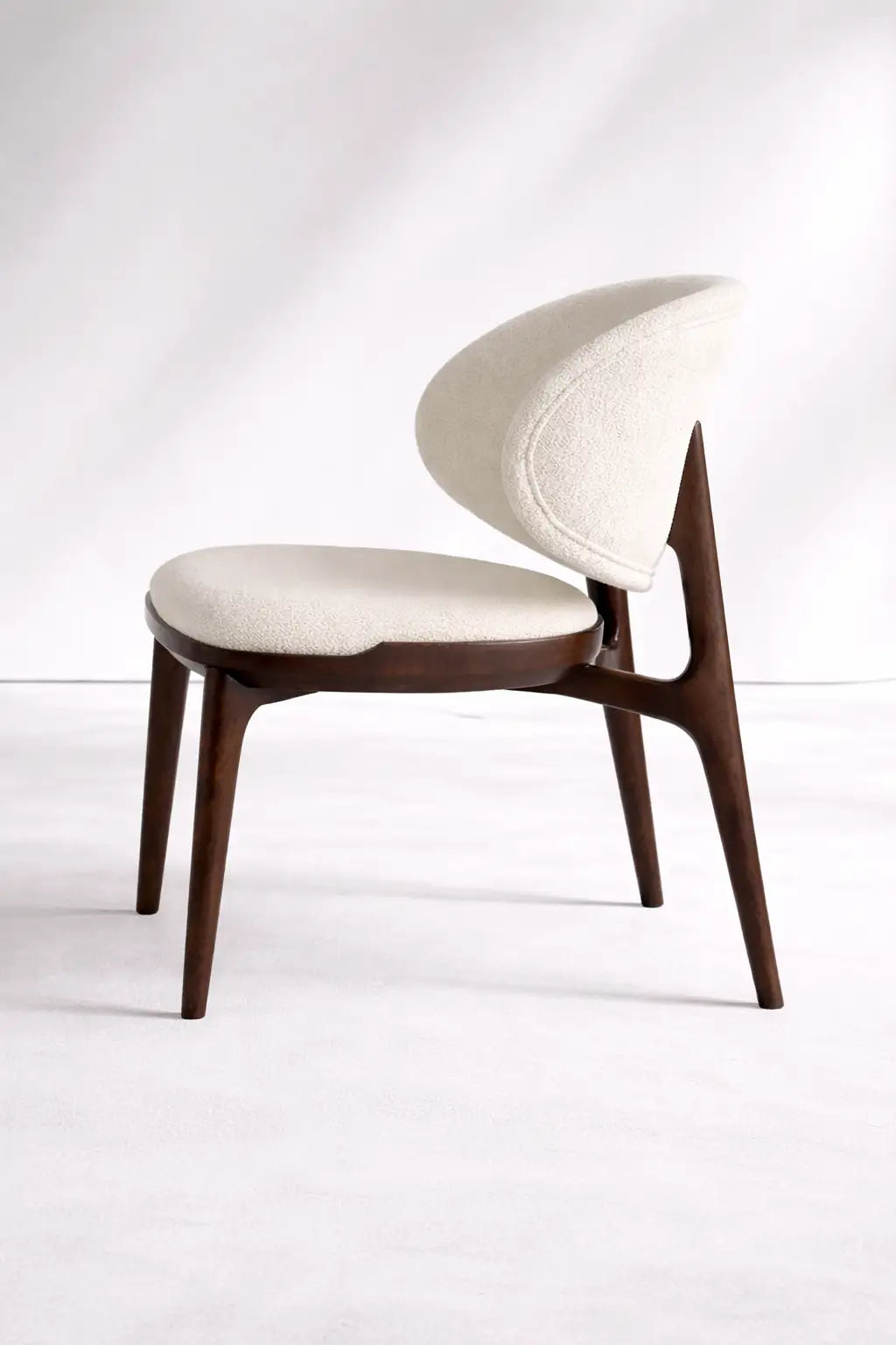 Side view of UK mid-century wooden chair featuring curved backrest, cream boucle upholstery and solid walnut frame.