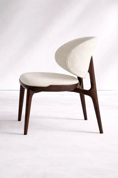 Side view of UK mid-century wooden chair featuring curved backrest, cream boucle upholstery and solid walnut frame.