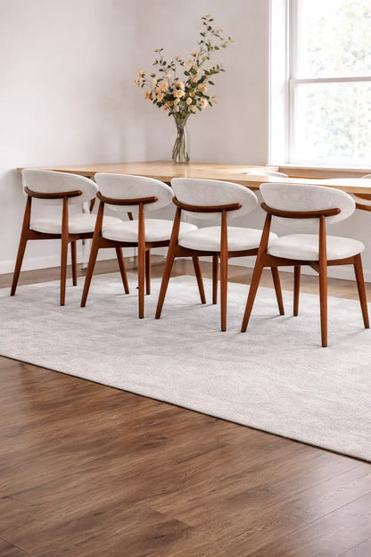 Set of walnut mid century dining chairs arranged around wooden dining table in bright UK dining room interior.