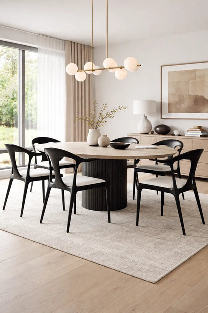 Set of six black wooden dining chairs around round table in bright modern UK dining room interior.